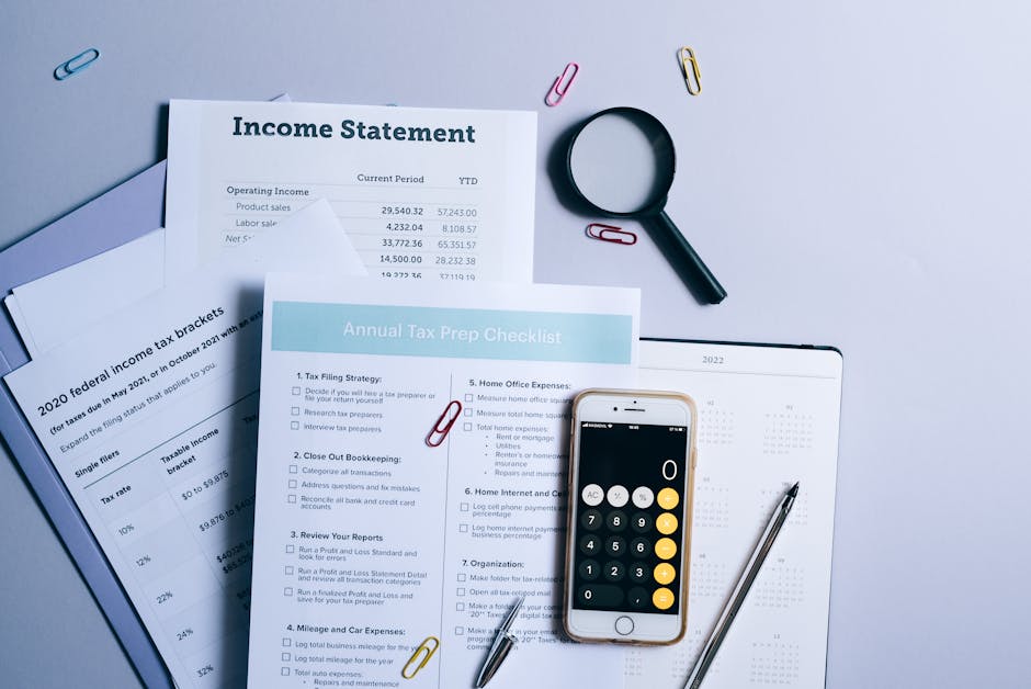 A flat lay of financial documents, including an annual tax prep checklist and a federal income tax brackets sheet, is arranged on a light-colored surface. The checklist features numbered items with ch